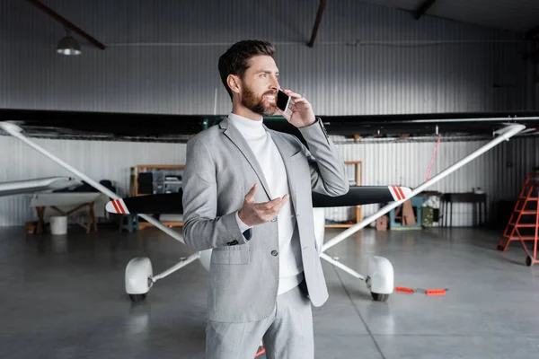 Glücklicher Mann in festlicher Kleidung, der in der Nähe eines modernen Hubschraubers mit dem Smartphone spricht und gestikuliert — Stockfoto