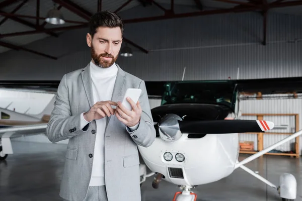 Uomo barbuto in giacca e cravatta utilizzando smartphone vicino elicottero moderno — Foto stock