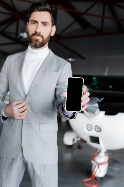 Homem de negócios em desgaste formal mostrando smartphone com tela em branco perto de helicóptero moderno — Fotografia de Stock