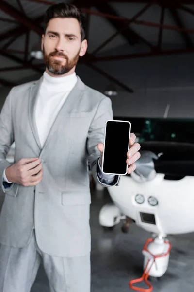 Businessman in formal wear showing smartphone with blank screen near modern helicopter — Stock Photo