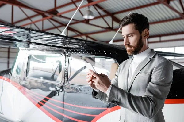 Bearded man in formal wear chatting on smartphone near modern helicopter — Stock Photo
