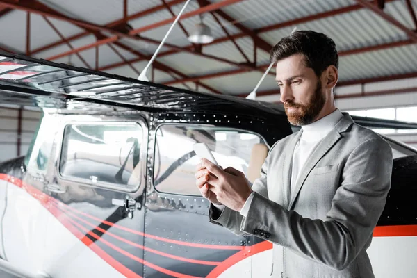 Hombre barbudo en desgaste formal charlando en el teléfono inteligente cerca de helicóptero moderno — Stock Photo