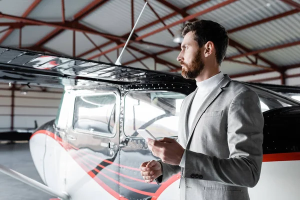 Distracted bearded man in formal wear holding smartphone near modern helicopter — Stock Photo