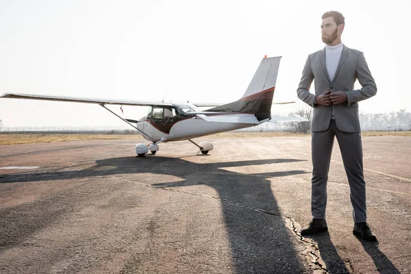 Longitud completa de hombre de negocios barbudo en traje de pie cerca de helicóptero al aire libre - foto de stock