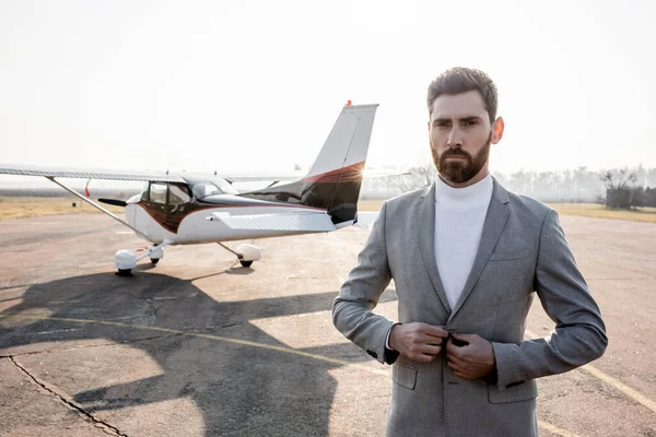 Confident businessman adjusting blazer and standing near helicopter outdoors — Stock Photo