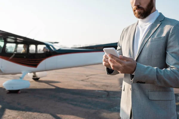 Cropped view of bearded businessman using smartphone near helicopter outdoors — Stock Photo