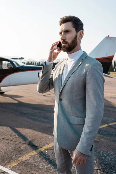 Hombre de negocios barbudo que tiene llamada telefónica en el teléfono inteligente cerca de helicóptero al aire libre - foto de stock