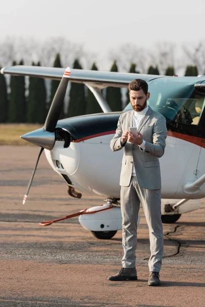 Comprimento total do empresário barbudo usando telefone celular perto de helicóptero ao ar livre — Fotografia de Stock