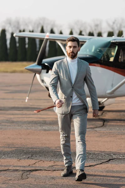 Longitud completa de hombre de negocios barbudo en desgaste formal caminando cerca de helicóptero al aire libre - foto de stock