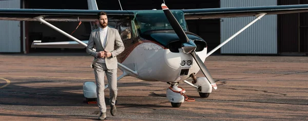 In voller Länge bärtiger Geschäftsmann im Anzug, der in der Nähe moderner Hubschrauber im Freien spaziert, Banner — Stockfoto