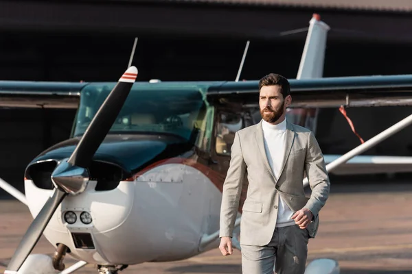 Homme d'affaires barbu en costume marchant près d'hélicoptère moderne et flou à l'extérieur — Photo de stock