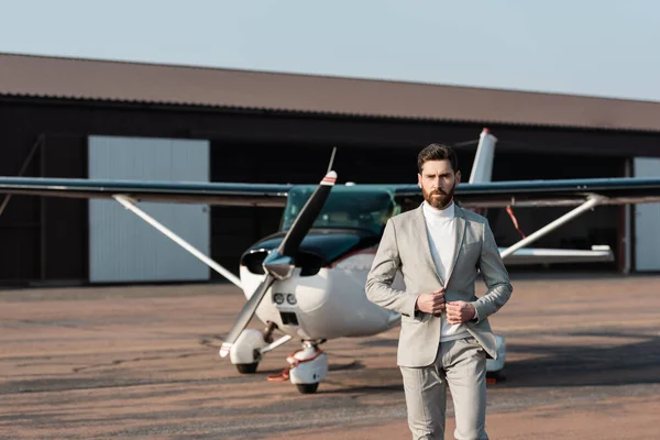 Homem de negócios barbudo ajustando blazer e andando perto de helicóptero moderno ao ar livre — Fotografia de Stock