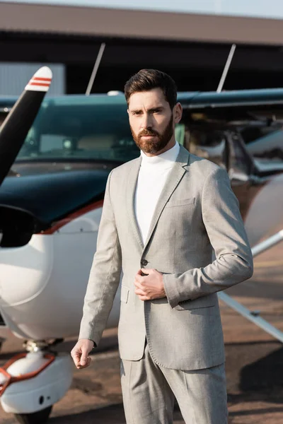 Bearded businessman adjusting blazer near blurred helicopter outdoors — Stock Photo
