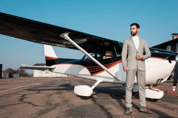 Selbstbewusster Geschäftsmann im Anzug steht neben modernem Hubschrauber und justiert Blazer — Stockfoto