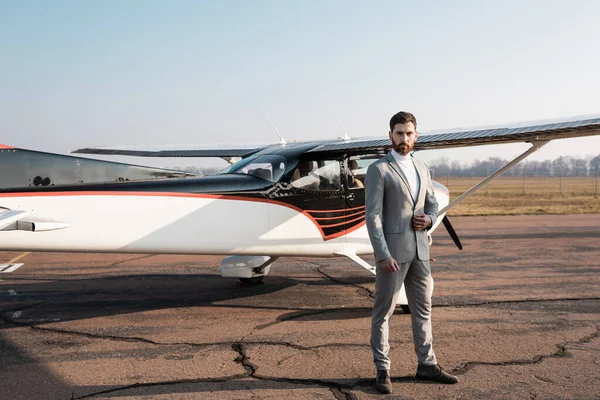 Selbstbewusster Geschäftsmann steht neben modernem Hubschrauber und justierendem Blazer — Stockfoto