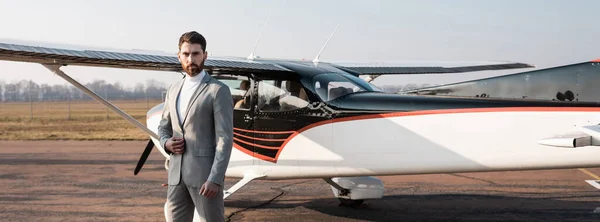 Empresário de sucesso em pé perto de helicóptero moderno e ajustando blazer, banner — Fotografia de Stock