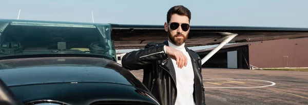 Pilote barbu en veste en cuir et lunettes de soleil debout près de l'hélicoptère, bannière — Photo de stock