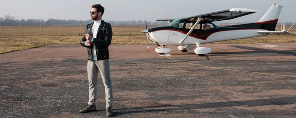 Piena lunghezza di pilota elegante in giacca di pelle e occhiali da sole in piedi vicino all'elicottero, banner — Foto stock