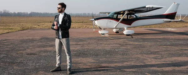 Toute la longueur du pilote élégant en veste en cuir et lunettes de soleil debout près de l'hélicoptère, bannière — Photo de stock