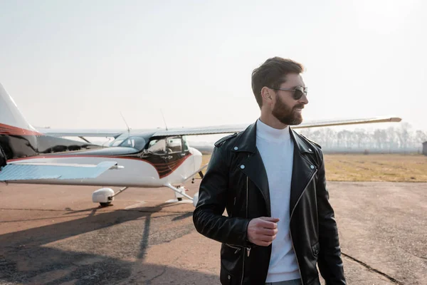 Piloto satisfecho en elegante chaqueta de cuero y gafas de sol cerca de helicóptero - foto de stock