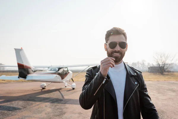 Pleased pilot in black leather jacket and sunglasses near helicopter — Stock Photo