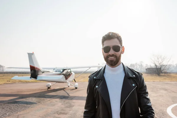 Piloto alegre en chaqueta de cuero negro y gafas de sol cerca de helicóptero - foto de stock