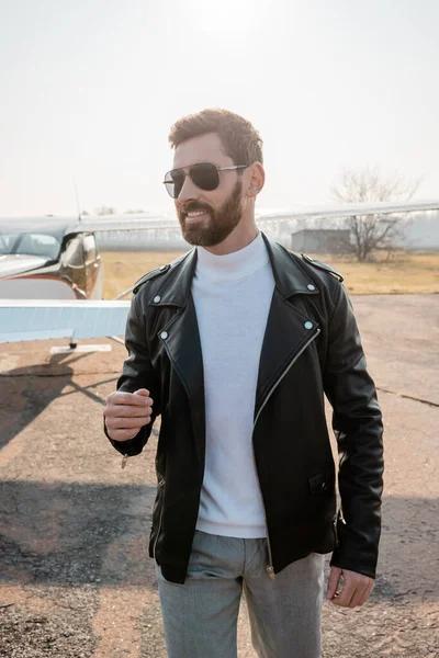 Piloto feliz en chaqueta de cuero y gafas de sol con estilo de pie cerca de helicóptero - foto de stock