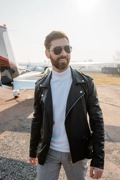 Pilote joyeux en veste en cuir et des lunettes de soleil élégantes debout près de l'hélicoptère — Photo de stock