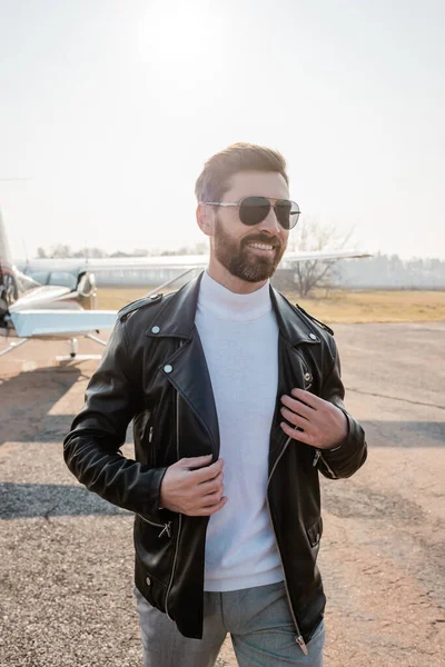 Smiling pilot in leather jacket and stylish sunglasses standing near helicopter — Stock Photo