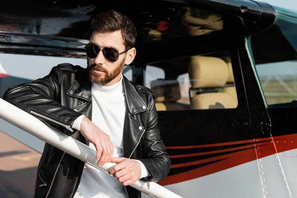 Confident man in sunglasses and black leather jacket near helicopter — Stock Photo