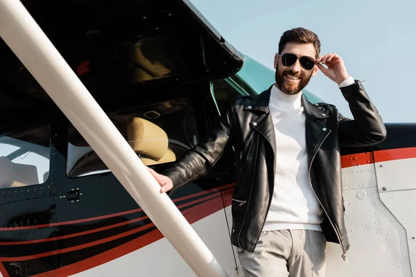 Веселий бородатий чоловік регулює сонцезахисні окуляри біля вертольота — стокове фото