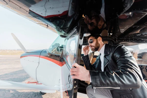 Bärtiger Pilot passt stylische Sonnenbrille an und öffnet Tür im Hubschrauber — Stockfoto