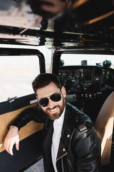 Positiver Pilot mit stylischer Sonnenbrille und Lederjacke in der Nähe der geöffneten Hubschraubertür — Stockfoto