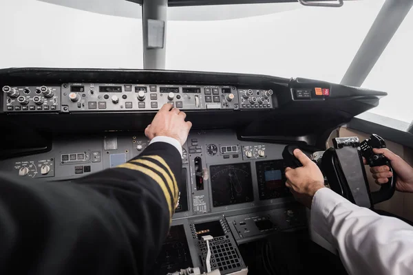 Cropped view of pilot reaching control panel near co-pilot using yoke in airplane simulator — Stock Photo