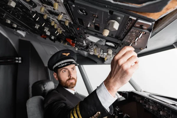 Pilot in cap and uniform reaching overhead panel in airplane simulator — Stock Photo