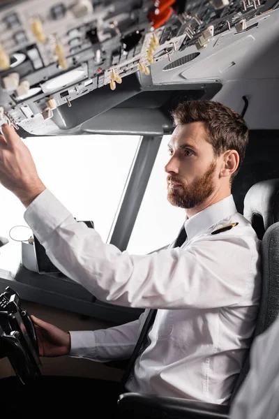 Bearded pilot reaching overhead panel while using yoke in airplane simulator — Stock Photo