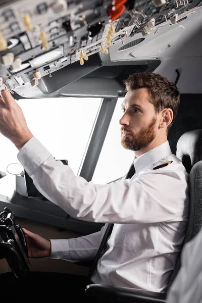 Piloto barbudo alcanzando el panel superior mientras usa yugo en simulador de avión - foto de stock