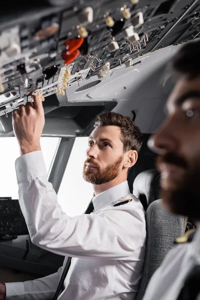 Bearded pilot reaching overhead panel near co-pilot in airplane simulator — Stock Photo