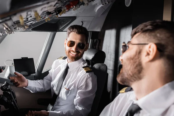 Cheerful pilots in sunglasses looking at each other in airplane — Stock Photo