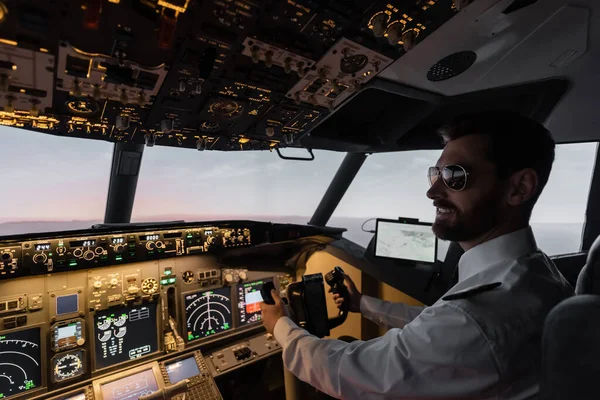 Cheerful pilot in sunglasses using yoke while piloting in evening — Stock Photo