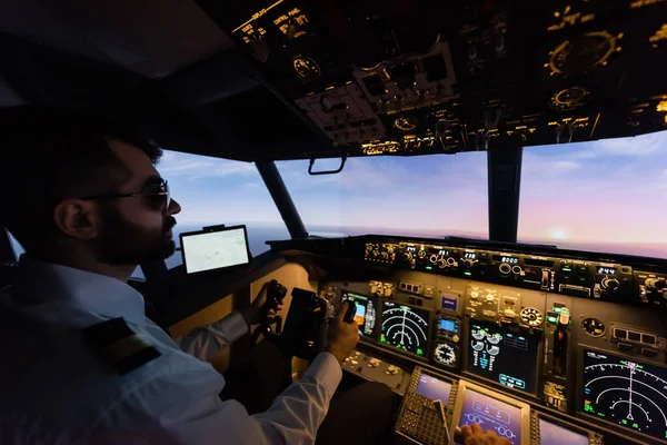 Бородатий пілот в сонцезахисних окулярах, використовуючи ярмо під час пілотування ввечері — стокове фото