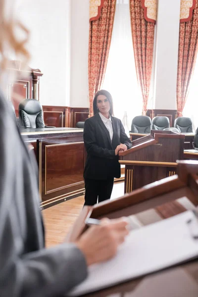 Brunette witness looking at blurred attorney writing during litigation — Stock Photo