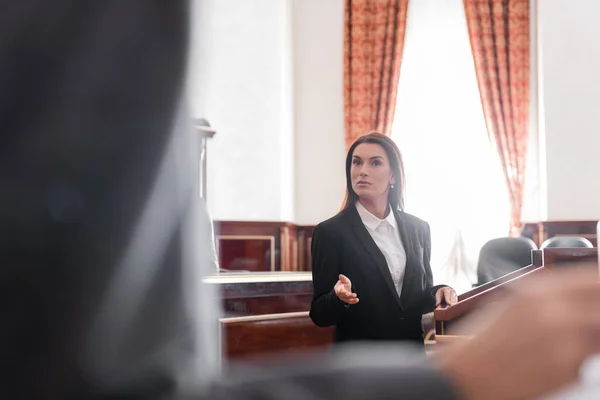 Brunette prosecutor pointing with hand while talking to blurred witness in courtroom — Stock Photo