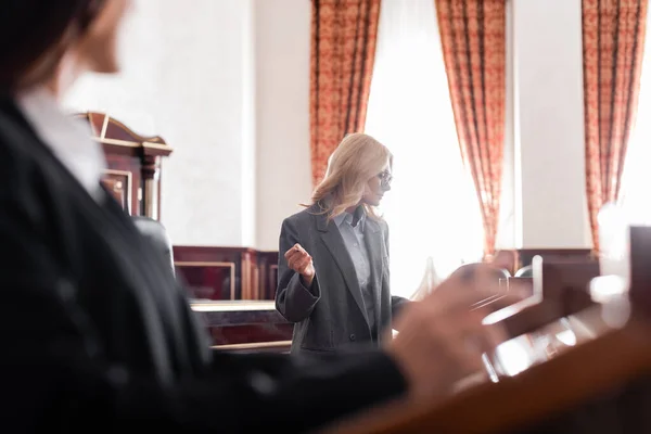 Middle aged advocate pointing with hand at blurred witness during questioning in court — Stock Photo