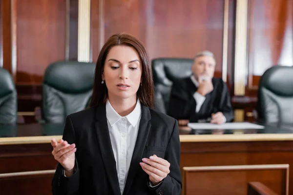 Brunette prosecutor pointing with finger during speech in courtroom near judge on background — Stock Photo