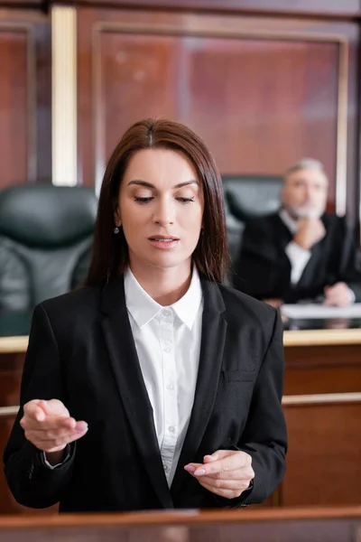 Prosecutor pointing with finger while talking in court near senior judge on blurred background — Stock Photo