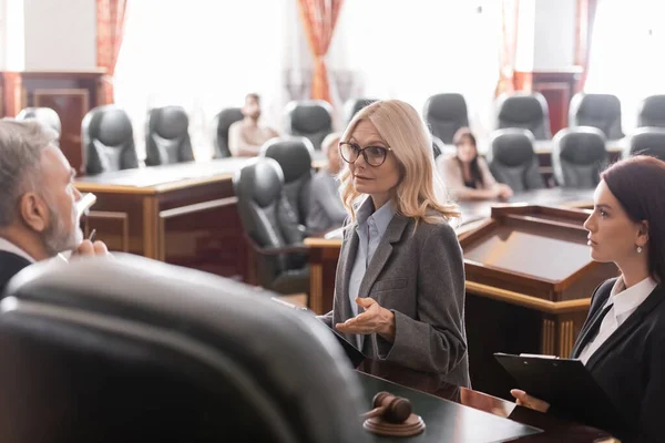 Abogado señalando con la mano mientras habla con el juez cerca del fiscal durante el litigio - foto de stock