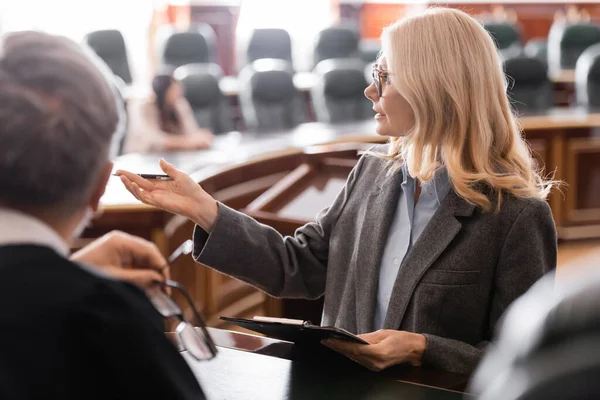 Middle aged attorney pointing with hand near grey-haired judge in courtroom — Stock Photo