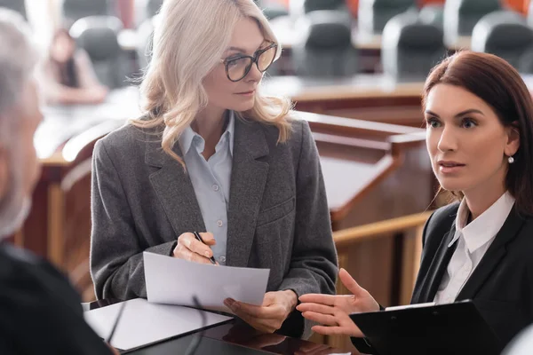 Prosecutor pointing with hand while talking to blurred judge near attorney in courtroom — Stock Photo