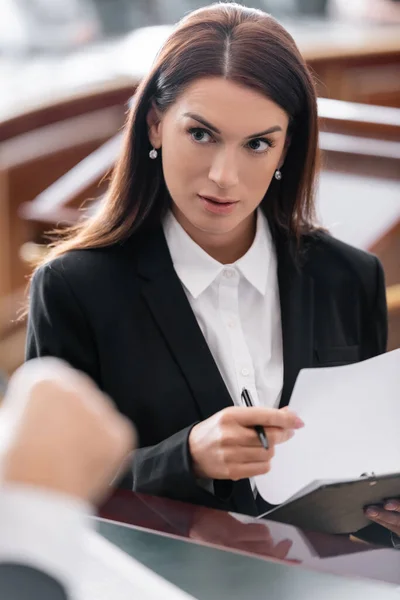 Brunette prosecutor looking at blurred judge while holding lawsuit in court — Stock Photo